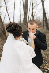 Fototapeta premium A bride and groom are standing in a forest, the bride is wearing a white dress and the groom is wearing a black suit