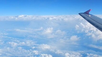 Flight over land and above white Stratocumulus low level clouds and Cumulus with view of blue sky horizon line and airplane wing. Topics: meteorology, air travel, vacation, space, atmosphere, airline