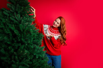 Photo of redhair smiling happy young girl wearing seasonal ugly sweater showing evergreen fir tree isolated on red color background