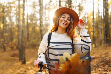 Young woman enjoys a sunny autumn day while riding her bicycle through a forest filled with colorful fallen leaves. Active lifestyle.