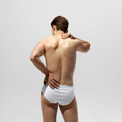 Back view of man stands holding one hand on his lower back, other on his neck, conveying sense of...