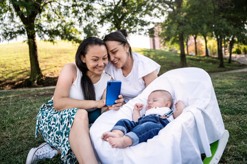Happy lesbian family enjoys outdoor time, capturing moments with their baby.