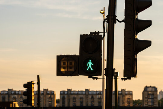 The image shows a traffic signal with a green pedestrian light in an urban environment during sunset, highlighting transportation and city life dynamics.