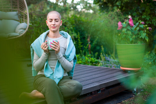 Young cancer patient sitting on garden patio with coffee, eyes closed. Health insurance, medical expenses, loss of income safety plan. Mental health, wellbeing, meditation during illness.