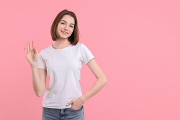 Happy teenage girl waving on pink background, space for text