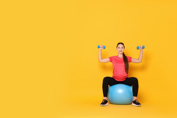 Beautiful pregnant woman with dumbbells doing exercises on fitball against yellow background, space for text