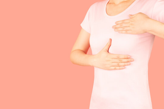 Woman palpating her breast by herself isolated on pink background. Breast self-exam for breast cancer awareness concept.