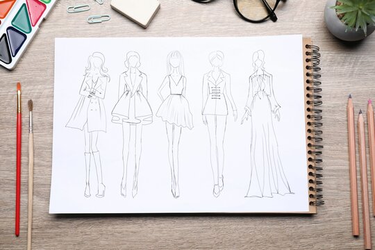 Sketch of stylish clothes and other fashion designer`s supplies on wooden table, flat lay