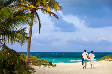 Picturesque view to tropical beach with white sand and coconut palm trees. Path to ocean coast, couple walking on tourist resort on Caribbean island