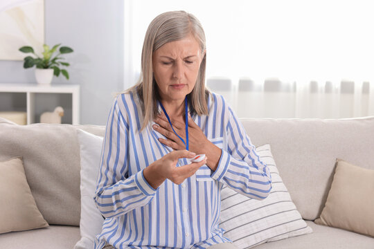 Senior woman suffering from heart pain pressing emergency call button at home