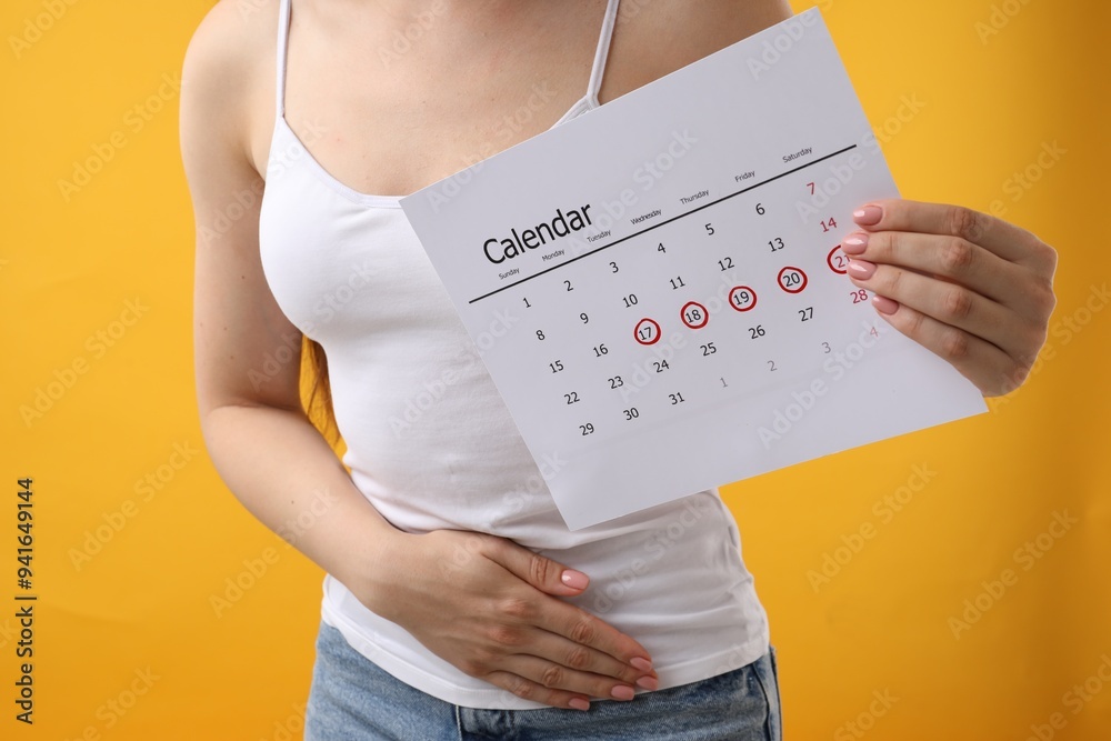 Canvas Prints Woman holding calendar with marked menstrual cycle days and suffering from abdominal pain on orange background, closeup