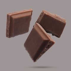 Pieces of sweet chocolate falling on grey background