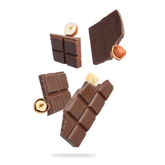 Pieces of tasty chocolate and hazelnuts falling on white background