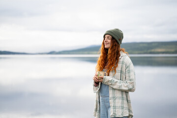 Serene young woman enjoying coffee by the lake