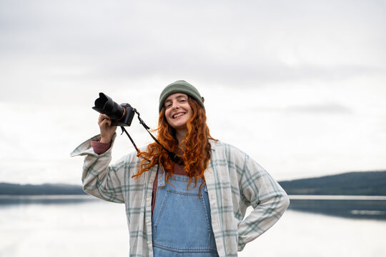 Smiling woman taking photos by a lake during camping