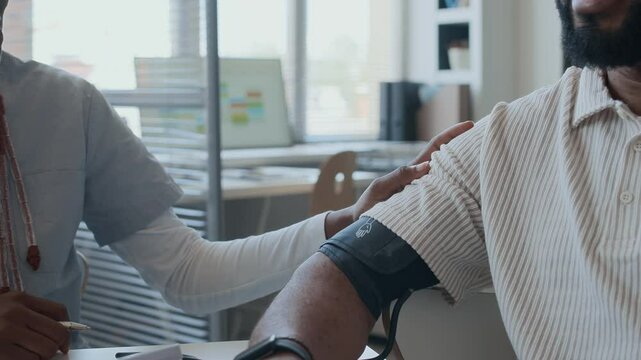 Close up view of positive female physician holding hand on male patients shoulder while measuring his blood pressure and communicating at appointment