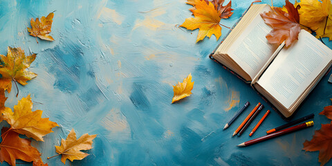 Open book with autumn leaves and pencils on a textured blue background