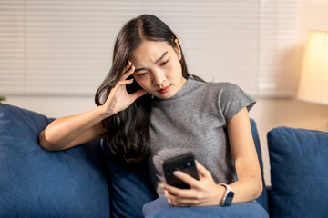 Young woman feeling stressed while using smartphone at home