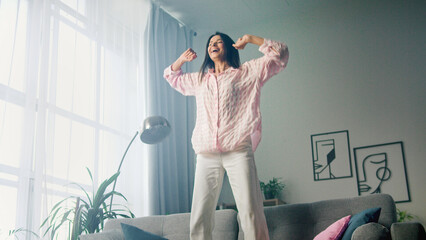 Woman enjoying music and dancing on sofa in living