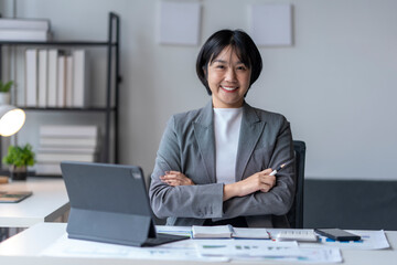 Asian businesswoman smiling at camera holding pen with arms crossed in office