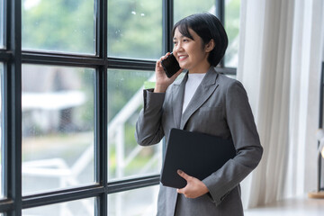 Fototapeta premium Businesswoman holding laptop having phone call looking through office window
