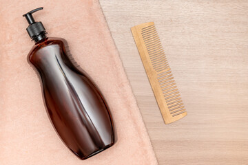 Brown container with dispenser. On a towel with a wooden comb. Top view.