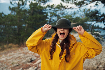 Woman in a stylish yellow raincoat and hat enjoying the scenic view from the hilltop surrounded by trees Travel fashion beauty nature concept