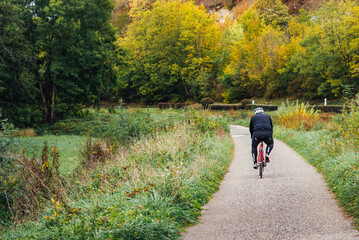Fototapeta premium Retraité faisant du vélo. Bicyclette en automne sur une piste cyclable. Balade en vélo en automne. Personne âgée sur un vélo. Vue arrière d'un sportif.