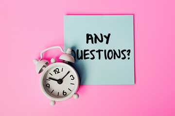 Sticky Note with 'Any Questions?' Written on It, Concept for Q&A Sessions, Inquiries, Customer Support, or Classroom Discussions. White alarm clock and Blue Note on a Pink Background