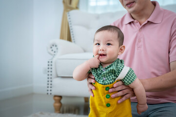 A man is holding a baby and smiling. The baby is wearing a yellow outfit. Scene is happy and joyful