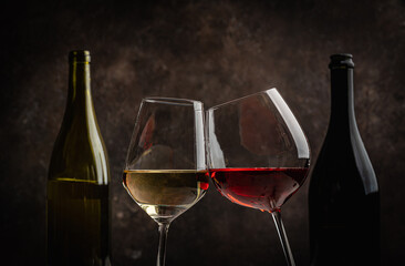 Glasses of red and white wine with bottles on dark rustic background