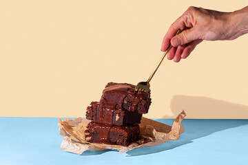 Hand pouring chocolate sauce on stacked brownies