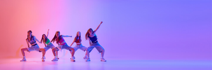 Banner. Group of young girls dancing in neon light against gradient pink background with negative space to insert text. Concept of sport and hobby, childhood, friendship, motion. Dance school.