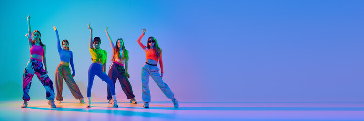 Banner. Teenage girls dancing hip-hop in neon light against gradient studio background with negative space to insert text. Concept of sport and hobby, childhood, friendship, motion. Dance lessons.