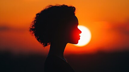 Close-up of a dramatic silhouette of a person standing against a setting sun, with warm orange and pink hues in the sky -
