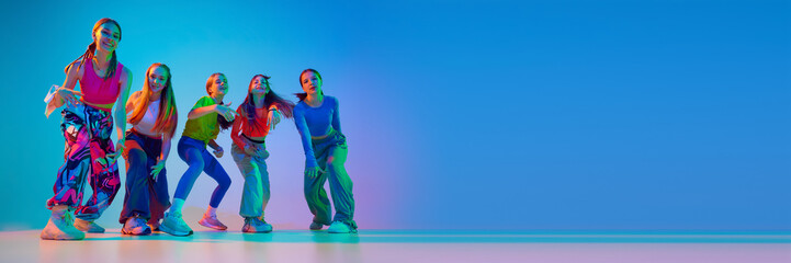 Fototapeta premium Dancers posing, showing their individuality throw moves in neon light against gradient background with negative space to insert text. Concept of sport and hobby, childhood, friendship, motion.