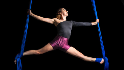 Female aerial dancer performing in blue silks against black