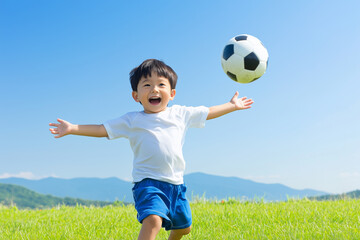 Obraz premium Joyful young boy playing soccer in an open grassy field on a sunny day, arms wide open with a big smile