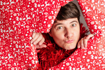 Woman peers playfully through Christmas-themed wrapping paper