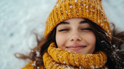 A serene and peaceful image of a young woman in a yellow knit hat lying on snowy ground, eyes closed and smiling gently, suggesting contentment and tranquility in the winter scene.