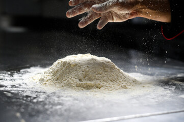 Baker clapping hands over heap of flour on metal counter