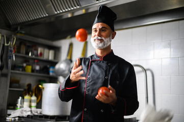 Senior chef juggling tomatoes in restaurant kitchen