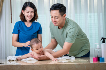 The father and mother are helping each other bathe their baby in a bathtub. In the picture, everyone looks happy.