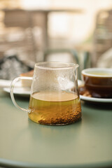 A glass teapot with buckwheat tea and a ceramic cup on the table on the summer terrace.