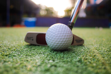 Putter and golf ball on green grass The scenery behind is mountains.