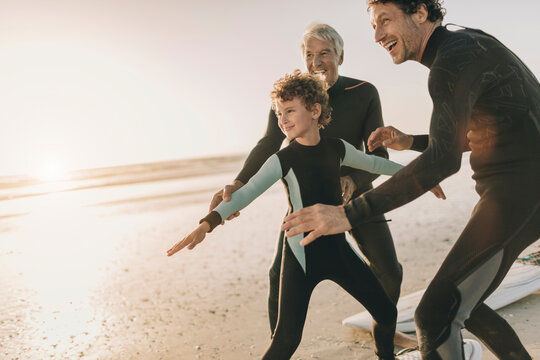 Three generations of men learning to surf on the beach at sunset