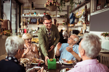 Restaurant owner giving gift to senior customers at cozy bistro