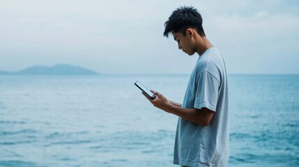 Young Asian Man Reviewing Financial Data and Technology Trends on a Tablet at the Beach During Daytime – Focused Work Amid Serene Sea Background