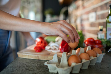 Woman reaching for an egg from a carton in the kitchen with fresh vegetables in the background