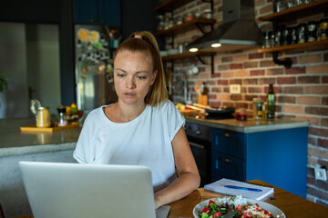 Young woman stressed while working from home on a laptop in kitchen